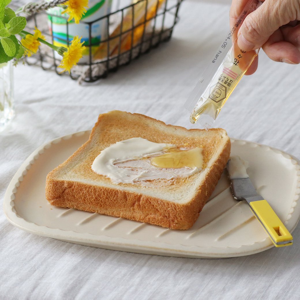トーストにスティックハチミツをかけているイメージ